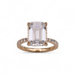 Rose gold ring with a large emerald-cut diamond and smaller diamonds on the band against a white background